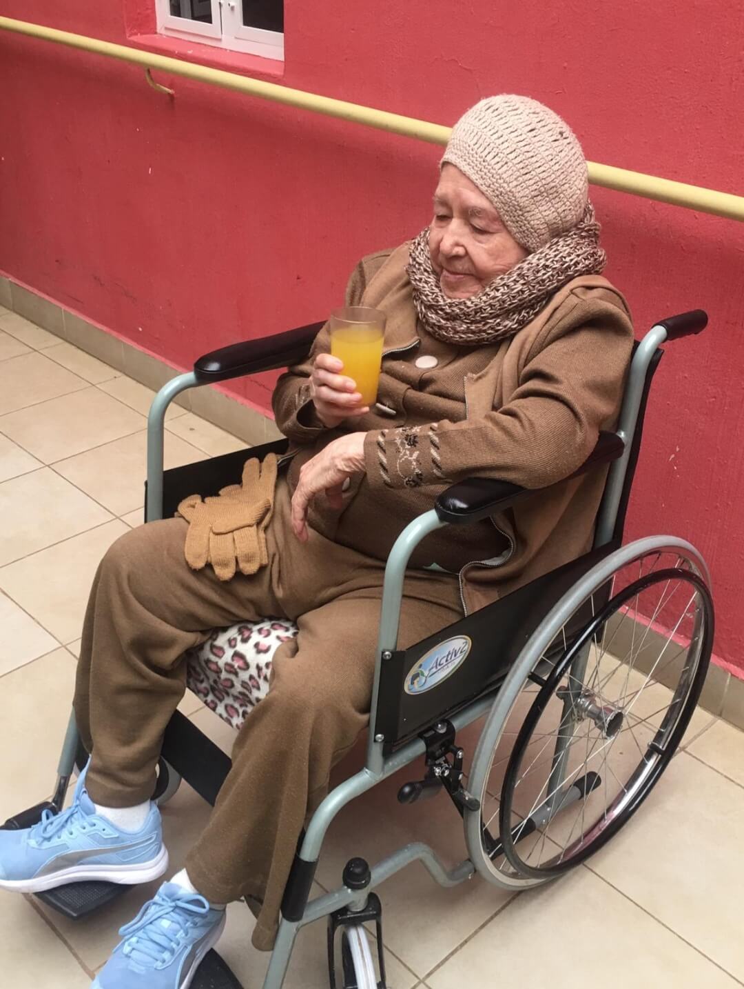 Elderly woman sitting in a wheelchair and drinking orange juice
